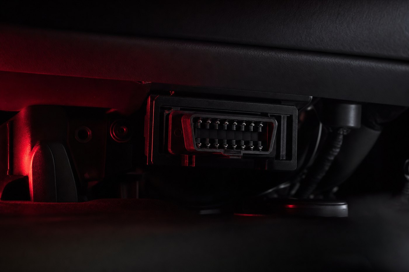 Close-up of a truck diagnostic port under the dashboard, its edges caught by a signal-red light